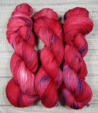 Hand-Dyed Yarn Scarlett Superwash Merino/Nylon is red with areas of blue and purple
