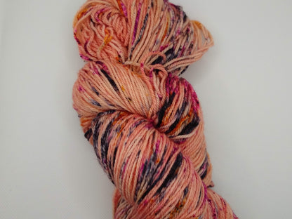 Hand-Dyed Yarn Fallen Angel a skein of peachy pink yarn with speckles of blued steel, berry crush and monarch orange.