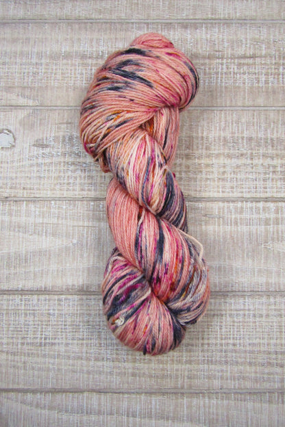 Hand-Dyed Yarn Fallen Angel a skein of peachy pink yarn with speckles of blued steel, berry crush and monarch orange.