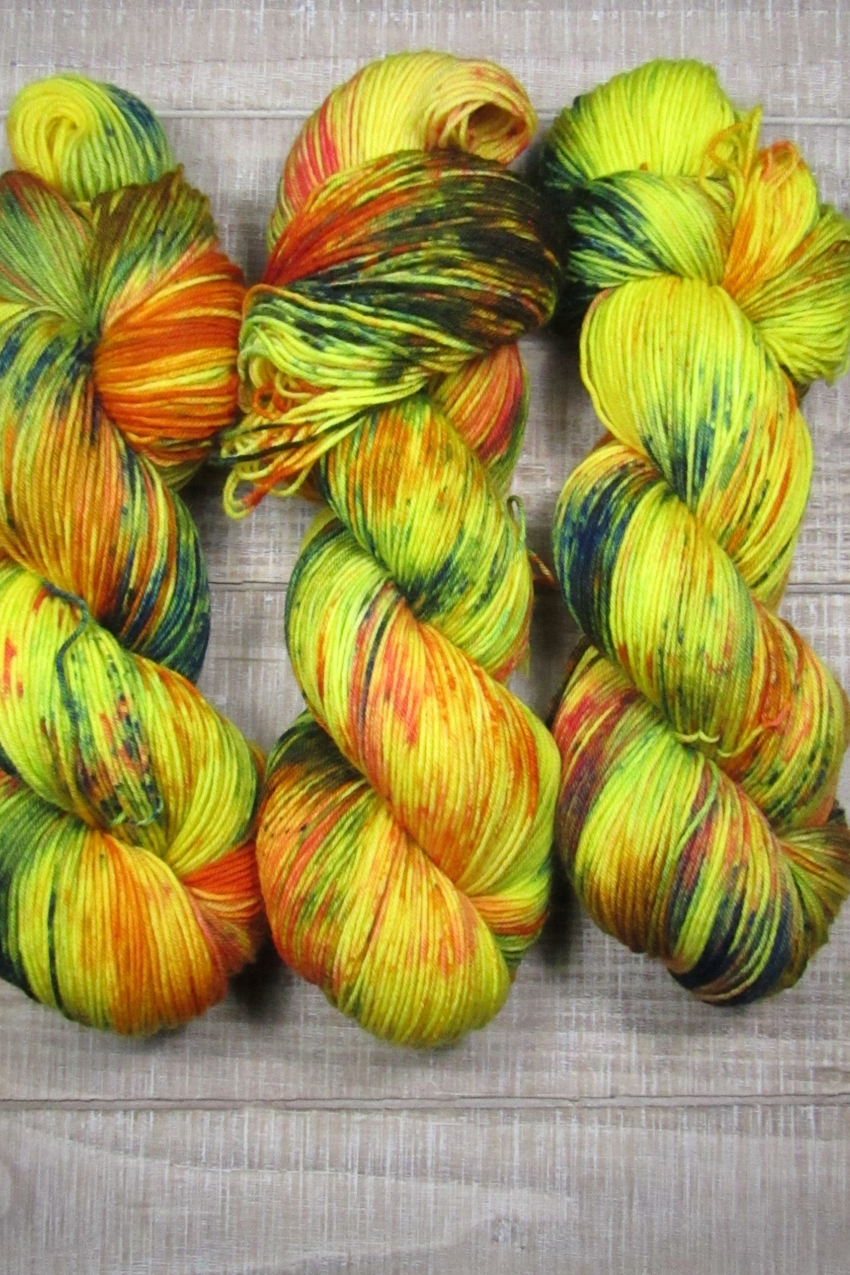 Hand-Dyed Yarn Sunny Superwash Merino/Nylon is a color of golden yellow with areas of orange, red, green, blue, and brown.