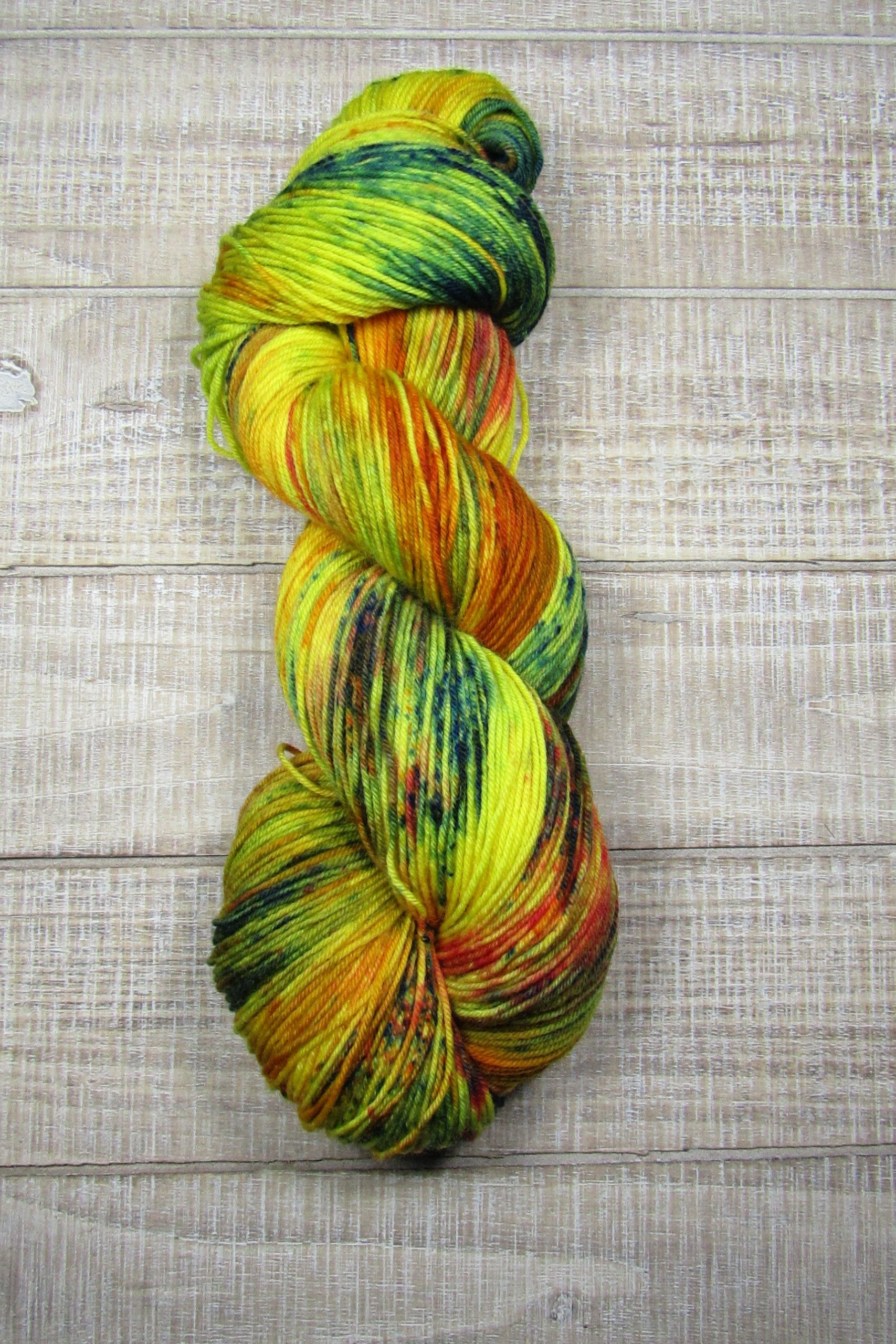Hand-Dyed Yarn Sunny Superwash Merino/Nylon is a color of golden yellow with areas of orange, red, green, blue, and brown.